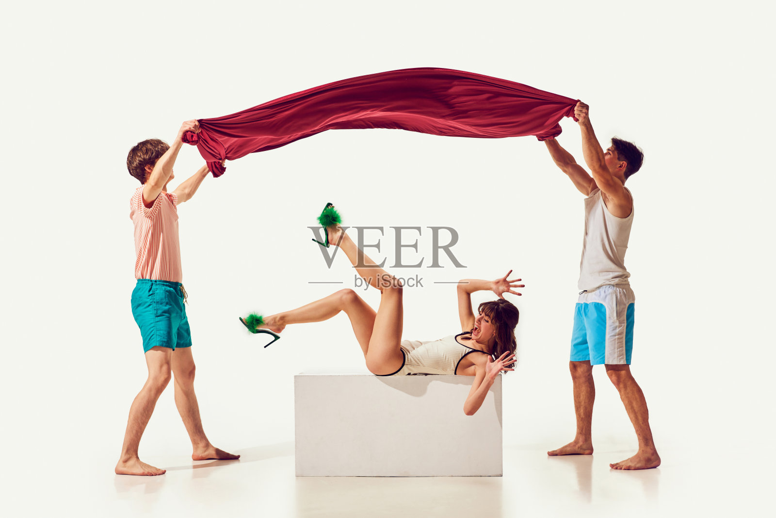 朋友们在海滩上玩耍。男人们把山毛榉毛巾放在穿着白色背景泳衣的年轻女子身上照片摄影图片