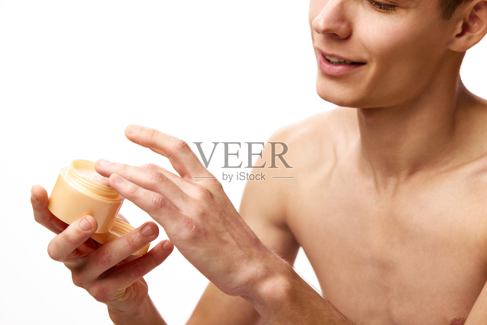 在白色的工作室背景下，赤裸上身的年轻男子拿着装有保湿霜的罐子照片摄影图片