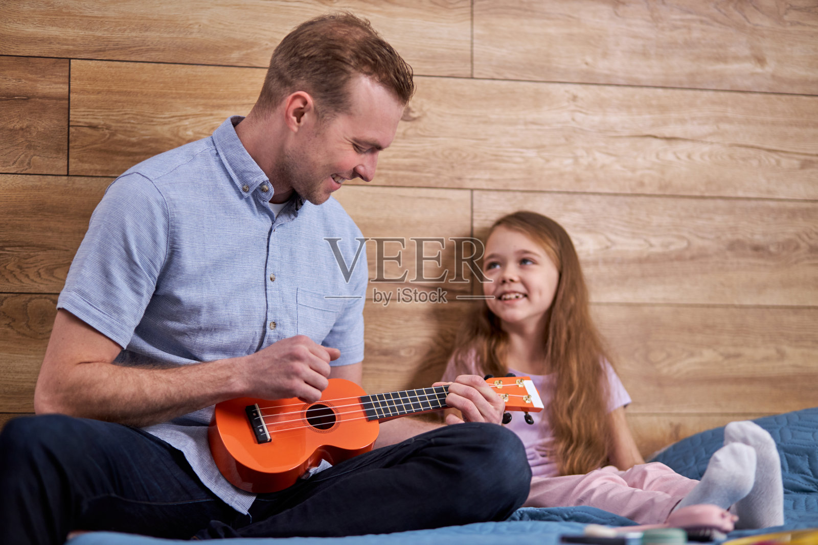 父亲和女儿弹吉他。小孩跟着家庭教师学习演奏乐器照片摄影图片