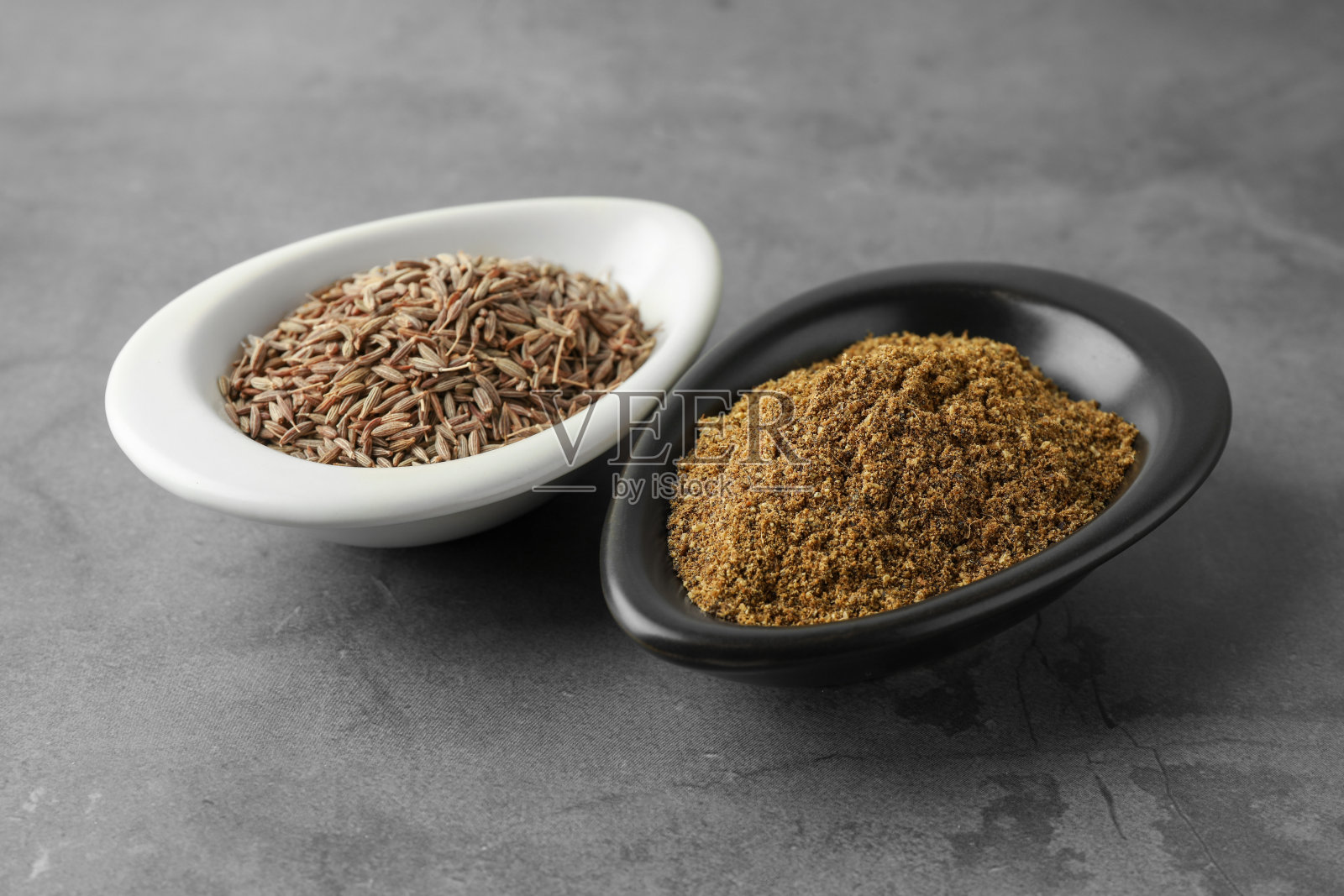 灰色桌子上的香菜(波斯孜然)粉末和干种子照片摄影图片