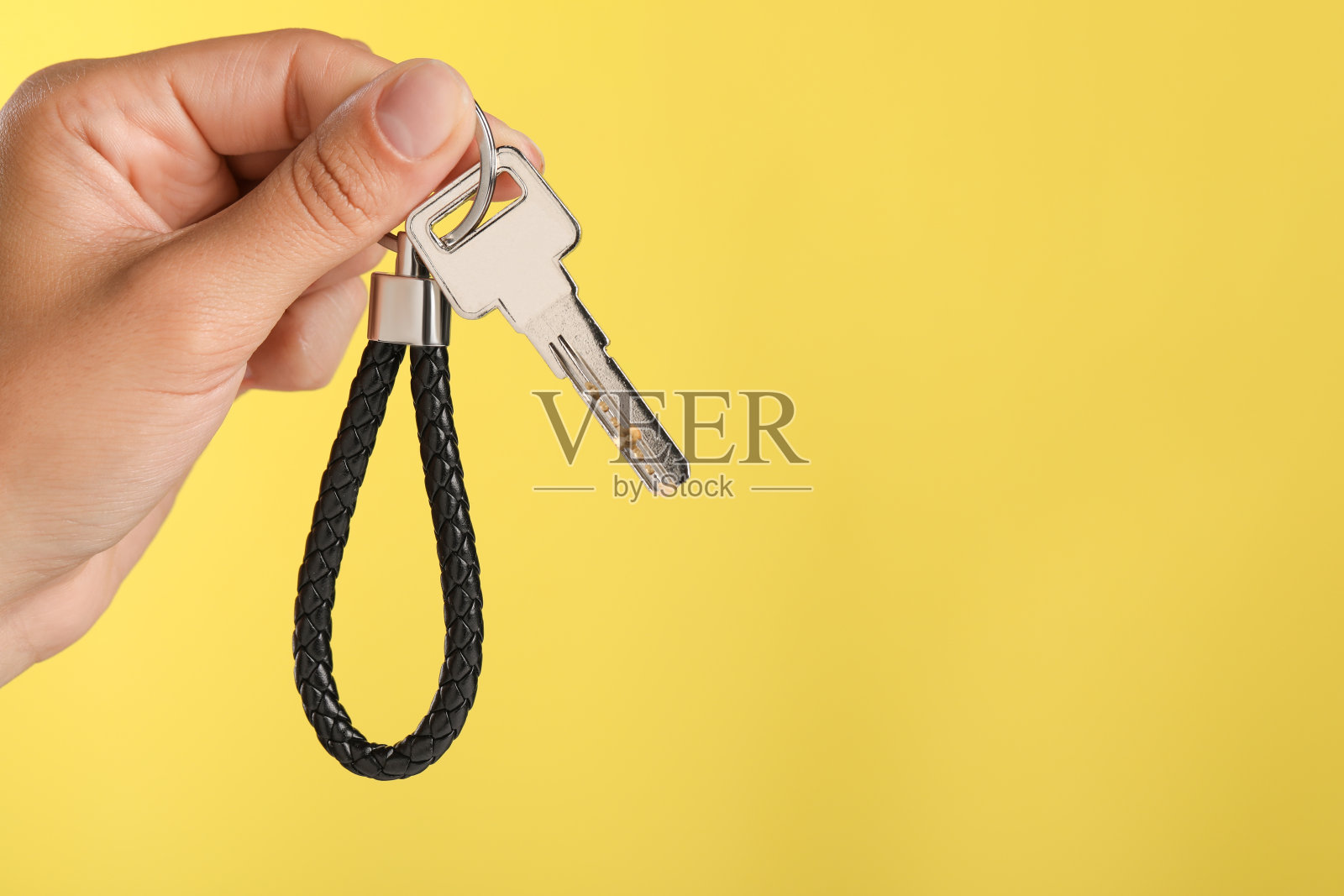 手持黄色背景黑色皮革钥匙链的女人，特写。文本空间照片摄影图片