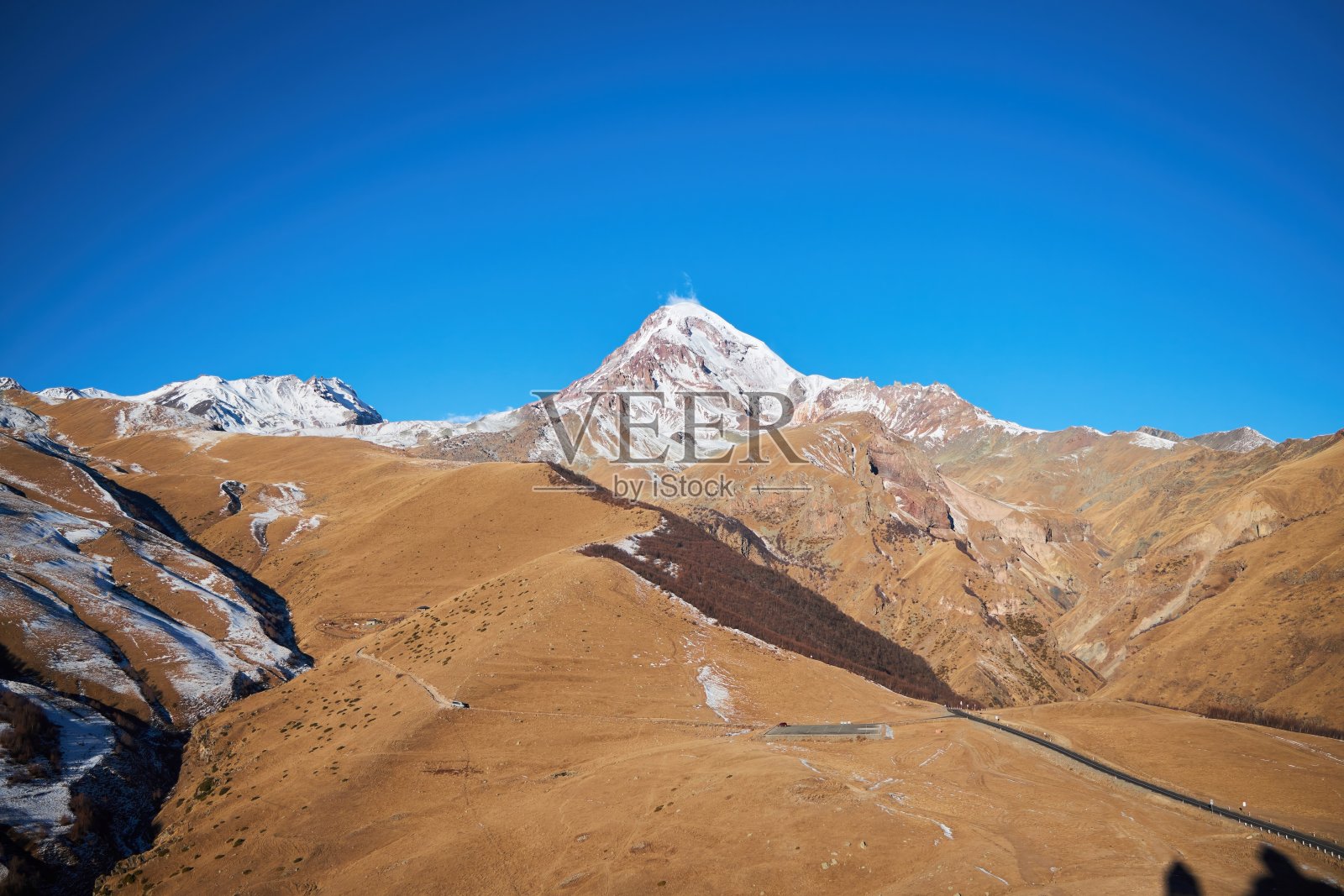 被太阳照亮的高山。风景与卡兹别克山顶和道路照片摄影图片