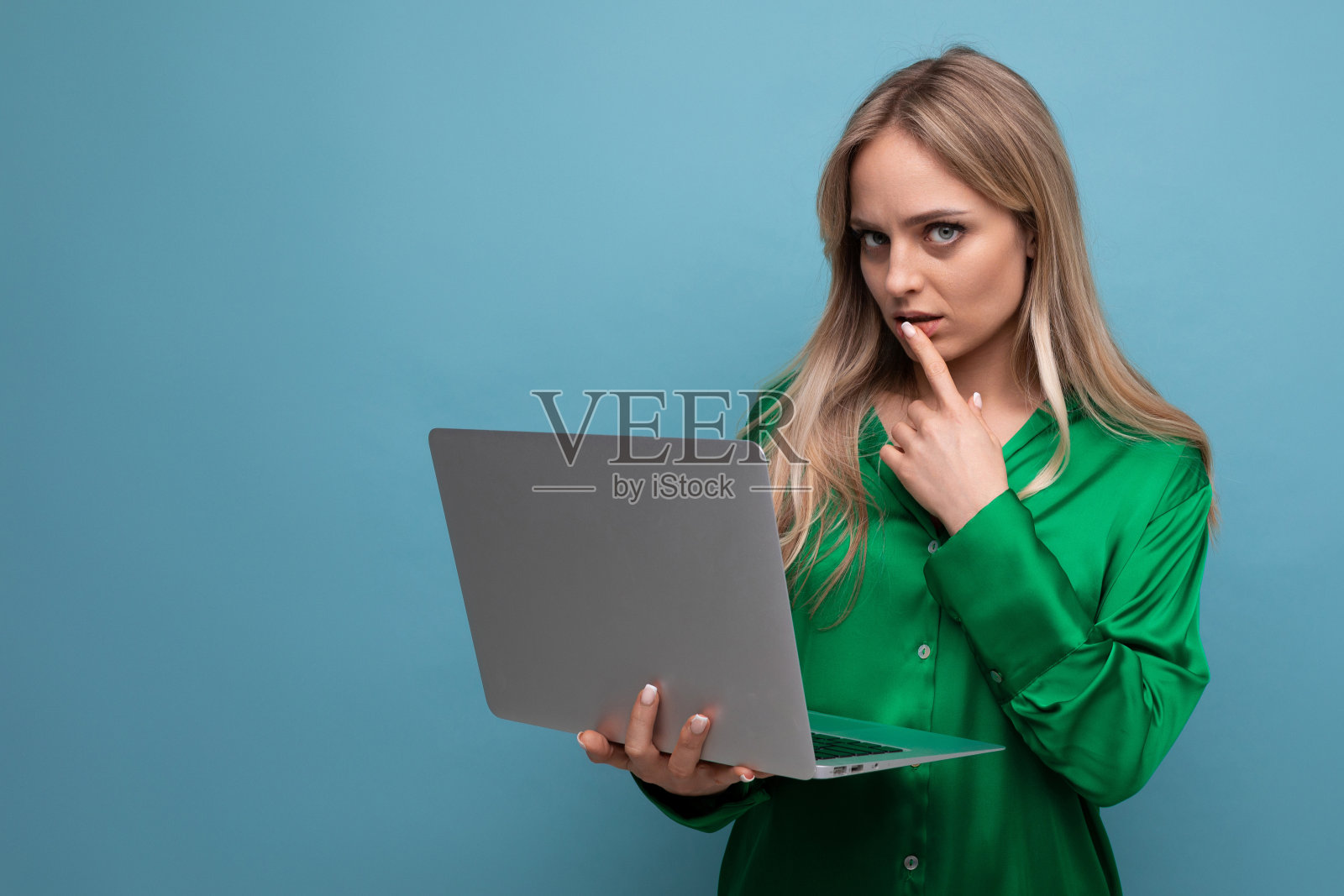 商务女性自由职业者手里拿着一台笔记本电脑，在蓝色明亮的背景下思考工作照片摄影图片