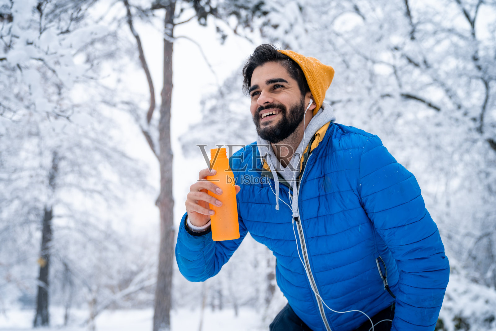 快乐微笑的男运动员在跑步后休息，拿着水瓶，看着远处照片摄影图片