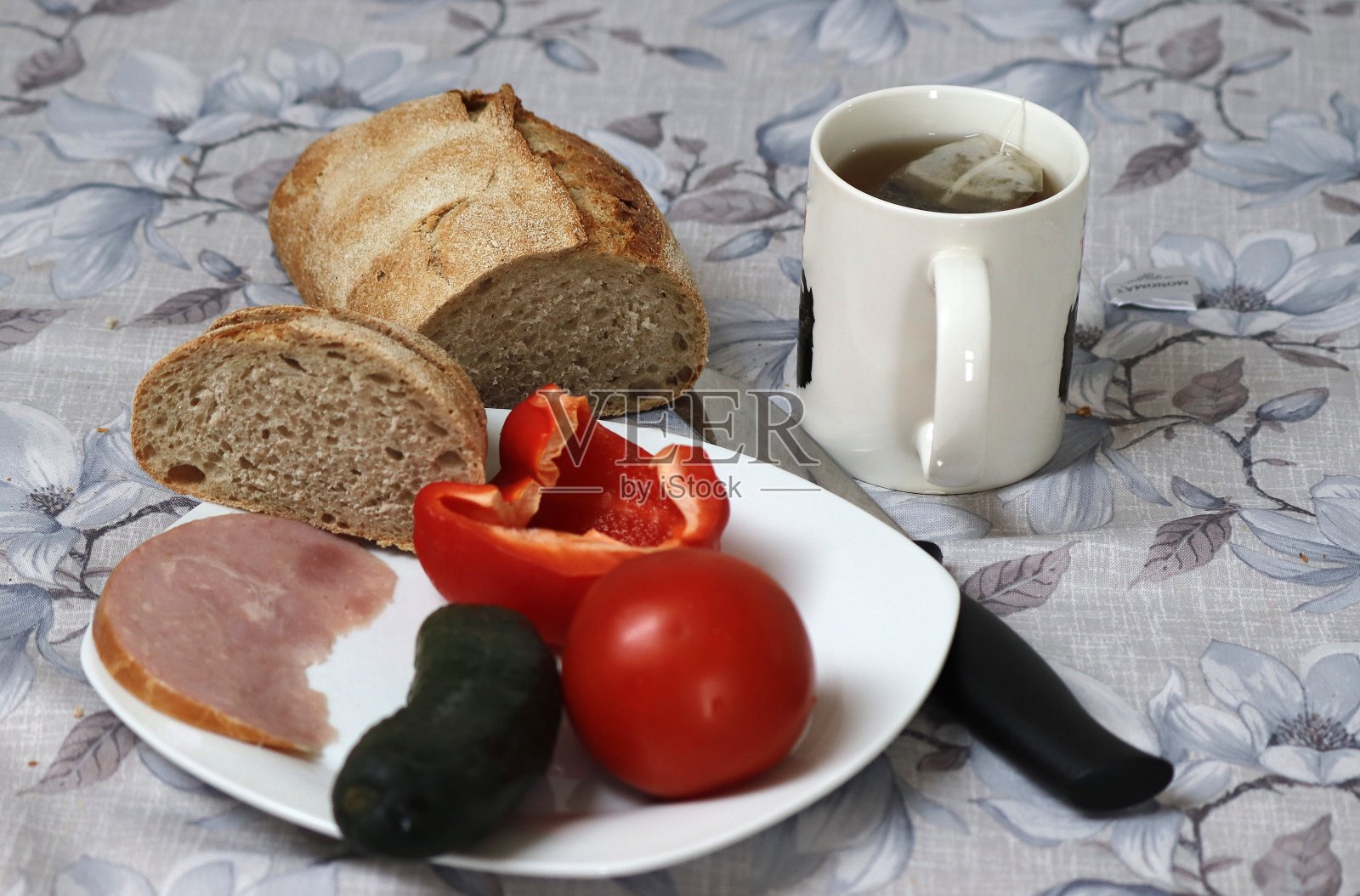 一个盘子里有黄瓜、番茄、甜椒、一块火腿，旁边是一杯茶，重点放在面包上。照片摄影图片