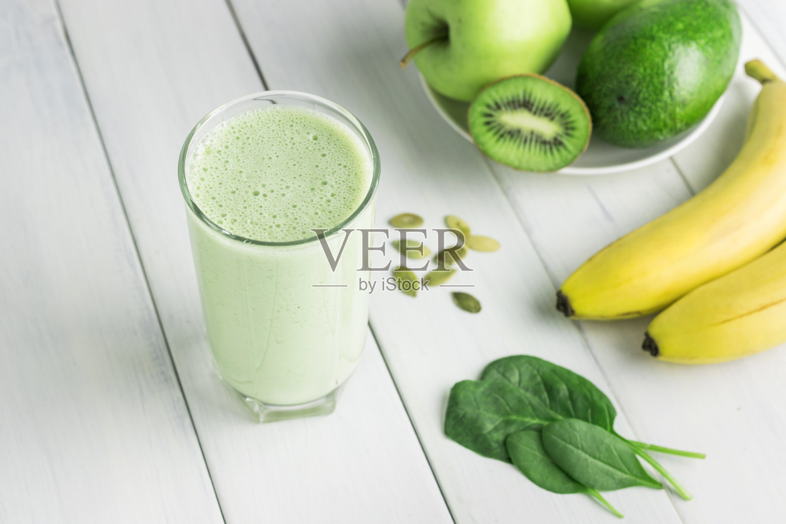 绿色排毒奶昔，将菠菜、苹果、香蕉、猕猴桃、鳄梨和种子放在白色木桌上，混合在一起的素食饮料，健康的饮食理念照片摄影图片