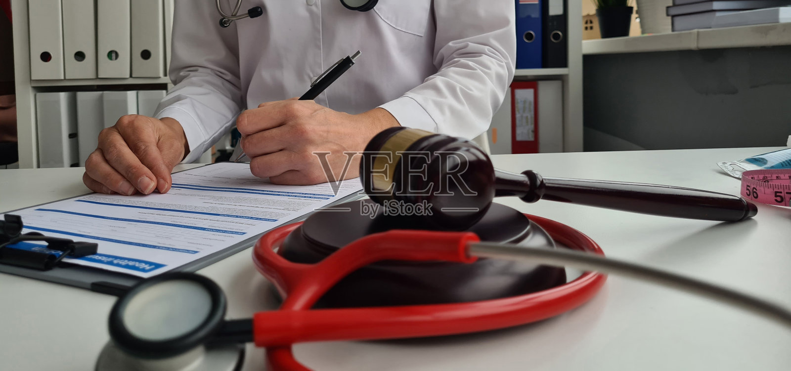 木制的法官木槌放在诊所的桌子上，医生在做文书工作照片摄影图片