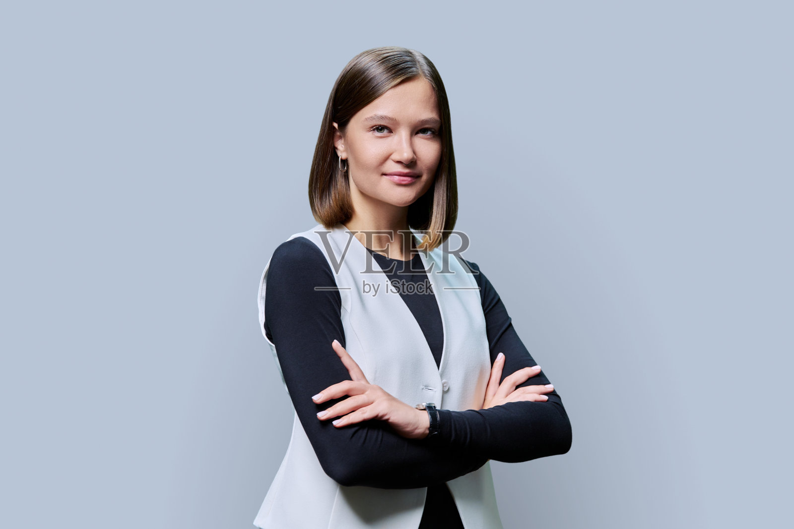 年轻自信的女人抱着双臂看着灰色背景下的相机照片摄影图片