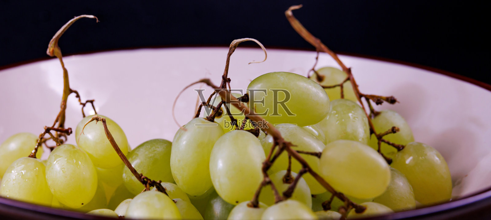 一小串漂亮的成熟的绿色葡萄放在一个深的陶瓷盘子里。照片摄影图片