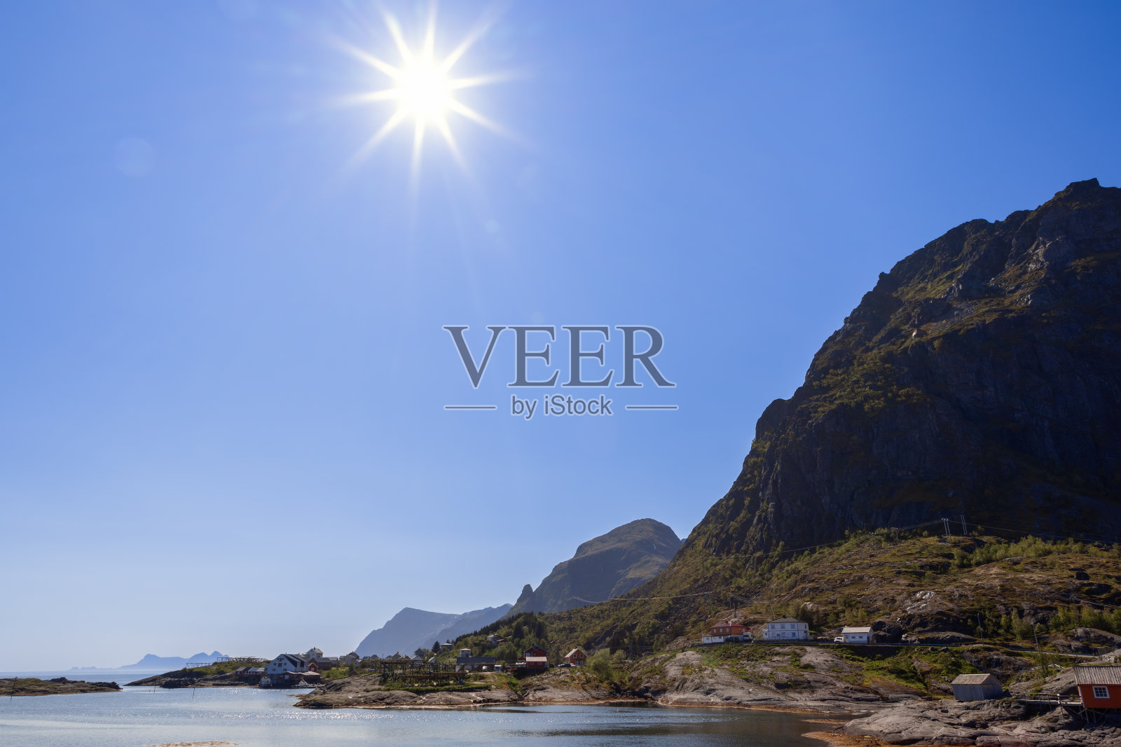 明亮的夏日阳光照亮了挪威罗弗敦群岛的莫斯科，在一个宁静、阳光明媚的日子里，清澈的蓝天下，绿色的山脉笼罩着房屋旁的经典鳕鱼烘干架，平静的大海照片摄影图片