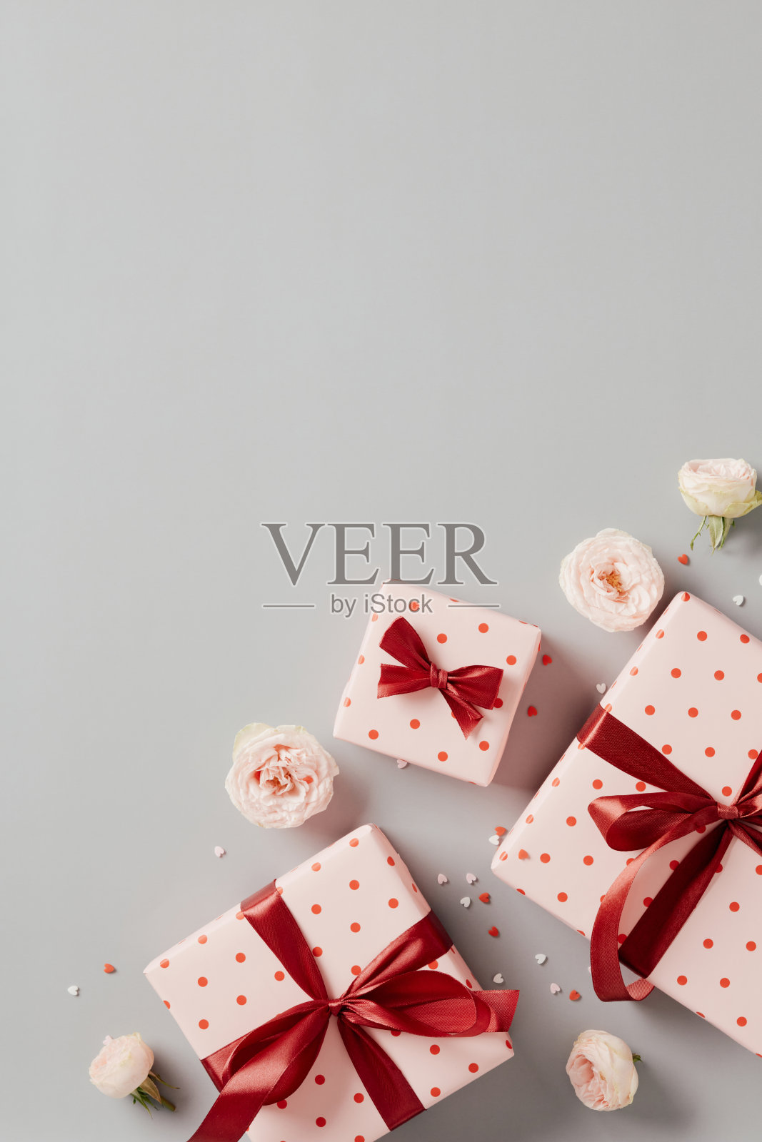 粉红色的礼物装饰的心和红丝带蝴蝶结，玫瑰花蕾，在灰色的背景彩纸。情人节快乐垂直背景。照片摄影图片