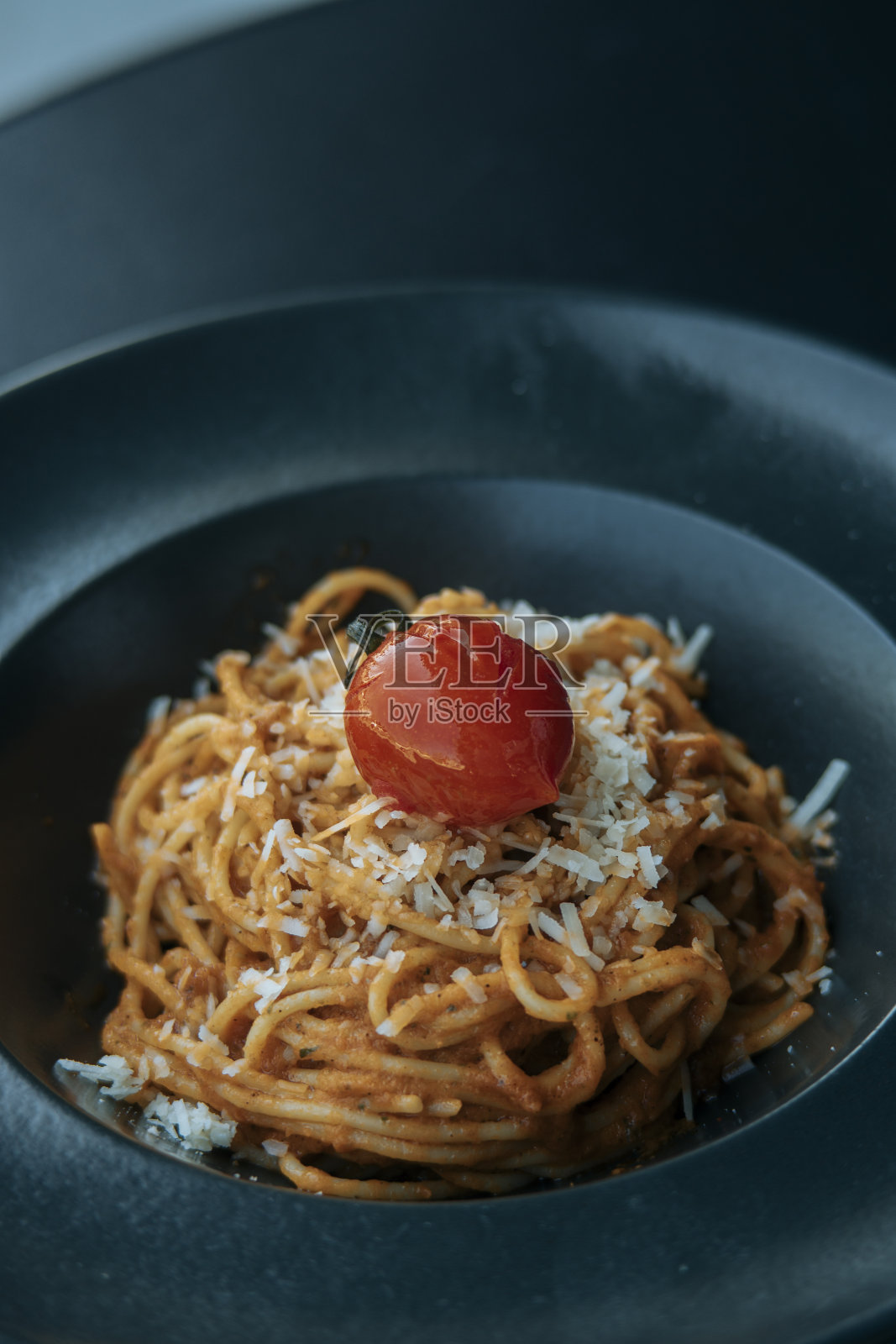 意大利面配上切达干酪和西红柿，装在黑色盘子里照片摄影图片