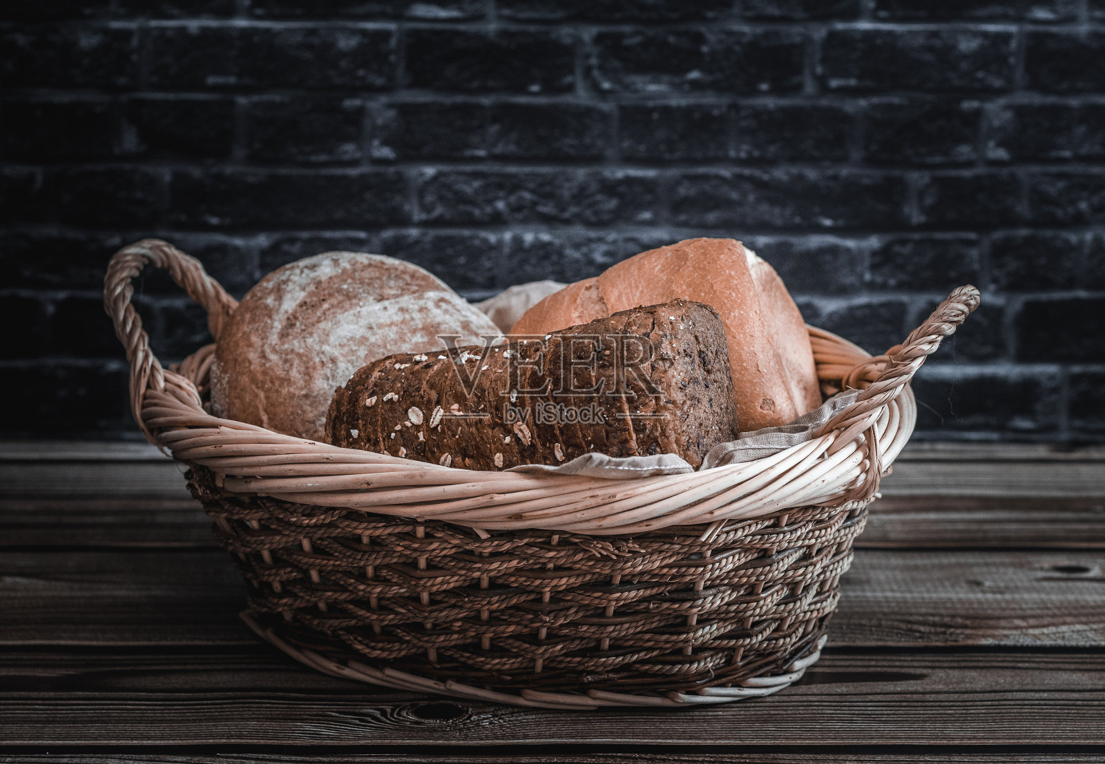 桌上的柳条篮子里放着三个不同品种的面包。照片摄影图片