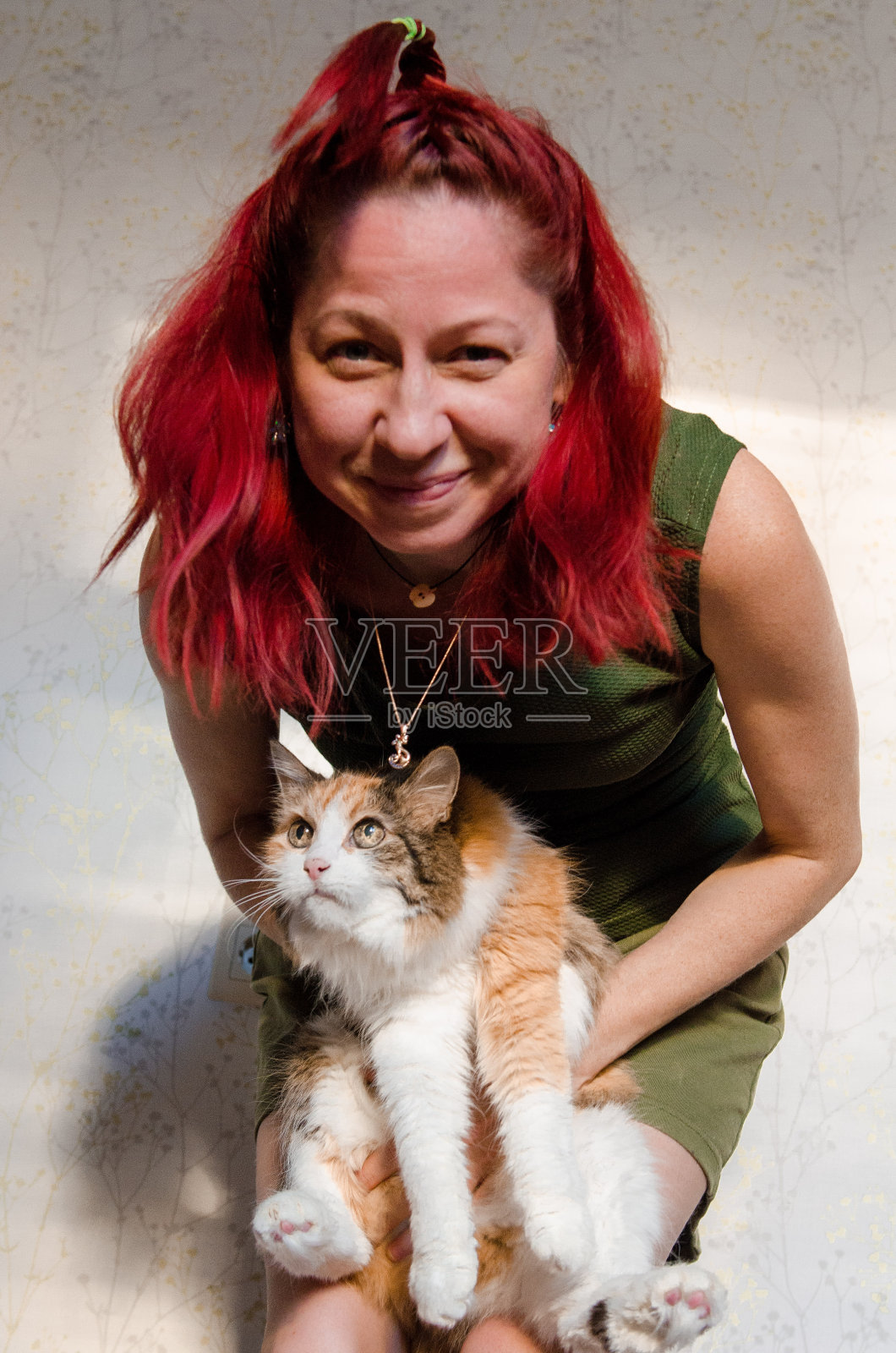 红发女孩和她可爱的印花猫。主人把宠物抱在手里。照片摄影图片