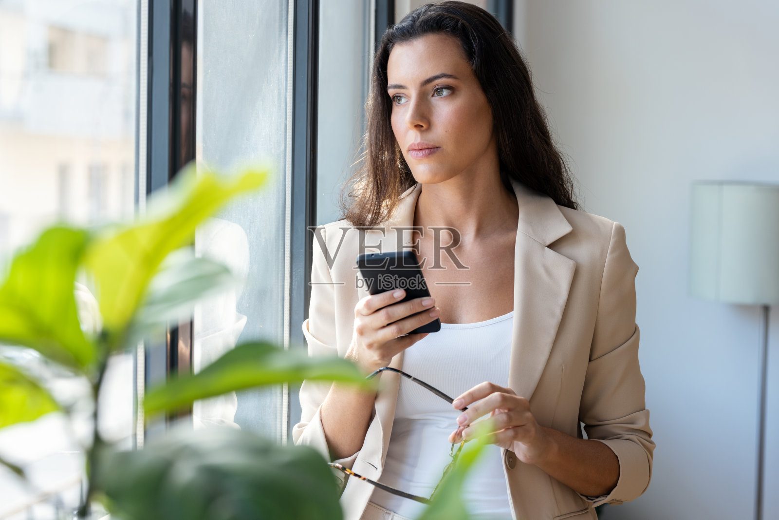 美女站在办公室的窗边玩手机照片摄影图片