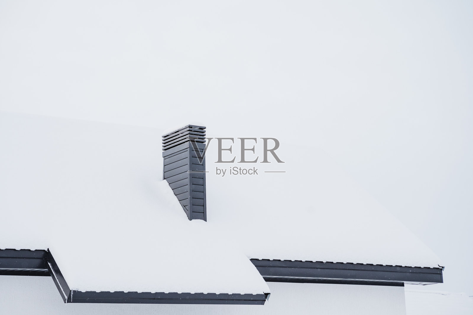 烟囱伸在房子的屋顶上，这是一个下雪的冬天，乡下房子的屋顶上撒满了雪，供暖管道。照片摄影图片