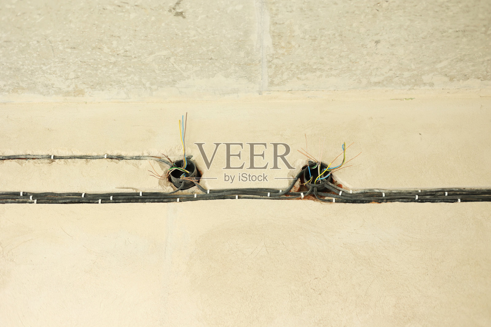 新公寓混凝土墙电缆布线。未完工的带电线的电源插座。新楼准备装修，家装维修。照片摄影图片