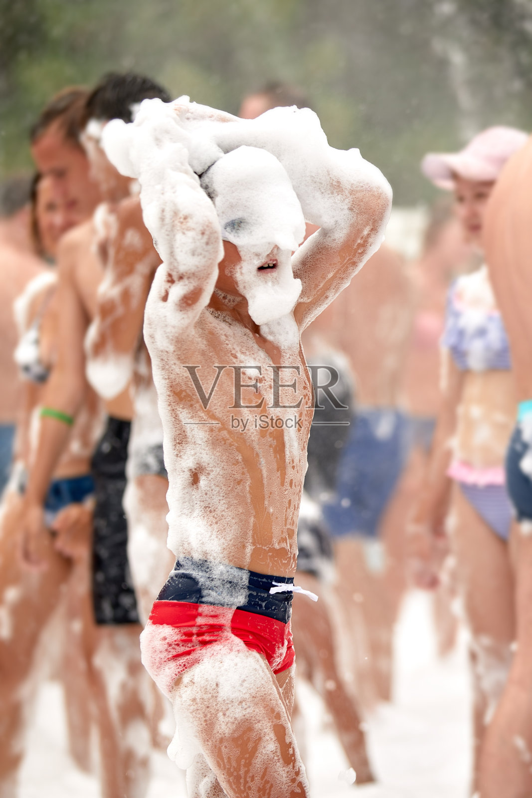 快乐的小男孩，头上有泡沫，在水上公园玩得很开心，在一个阳光明媚的炎热的夏天，穿着湿泳衣参加泡沫派对或度假照片摄影图片