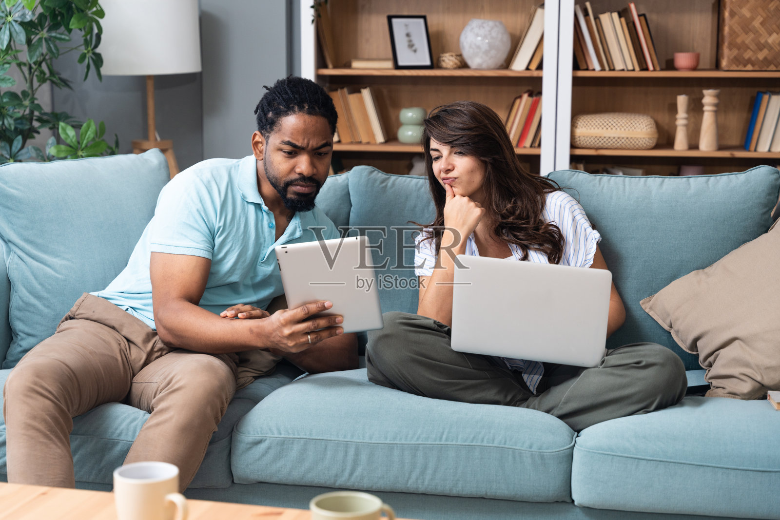 年轻的商业伙伴在家里办公室一起工作，坐在沙发上使用笔记本电脑和平板电脑。小公司老板工作，互联网创业家互相展示创意。照片摄影图片