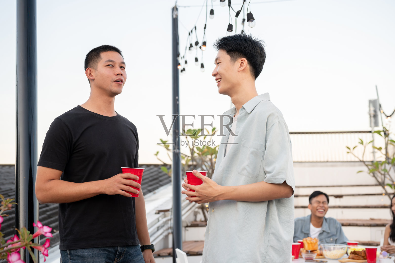 两个快乐的年轻亚洲男性朋友在屋顶酒吧聚会时谈笑风生。照片摄影图片