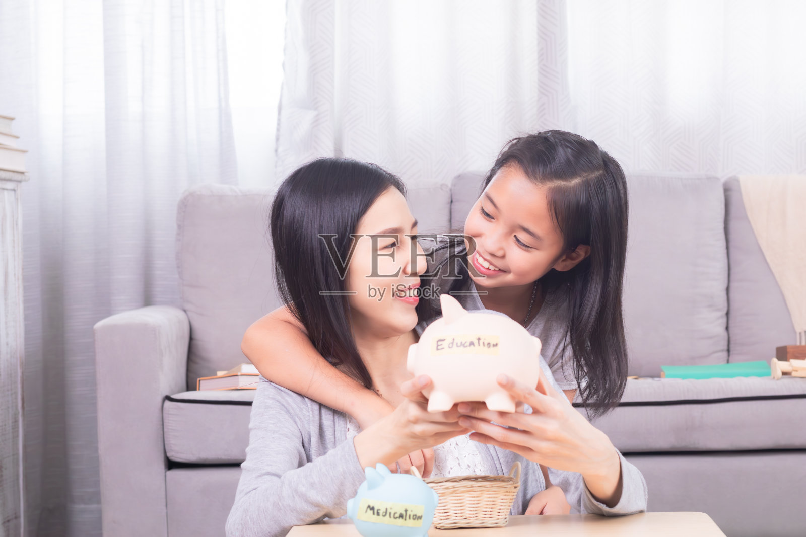 亚洲妈妈把硬币放在储蓄罐里，为孩子的医药费和教育费存钱，生活理念，很好地组织有两个孩子的单身妈妈的财务和住房开支规划照片摄影图片