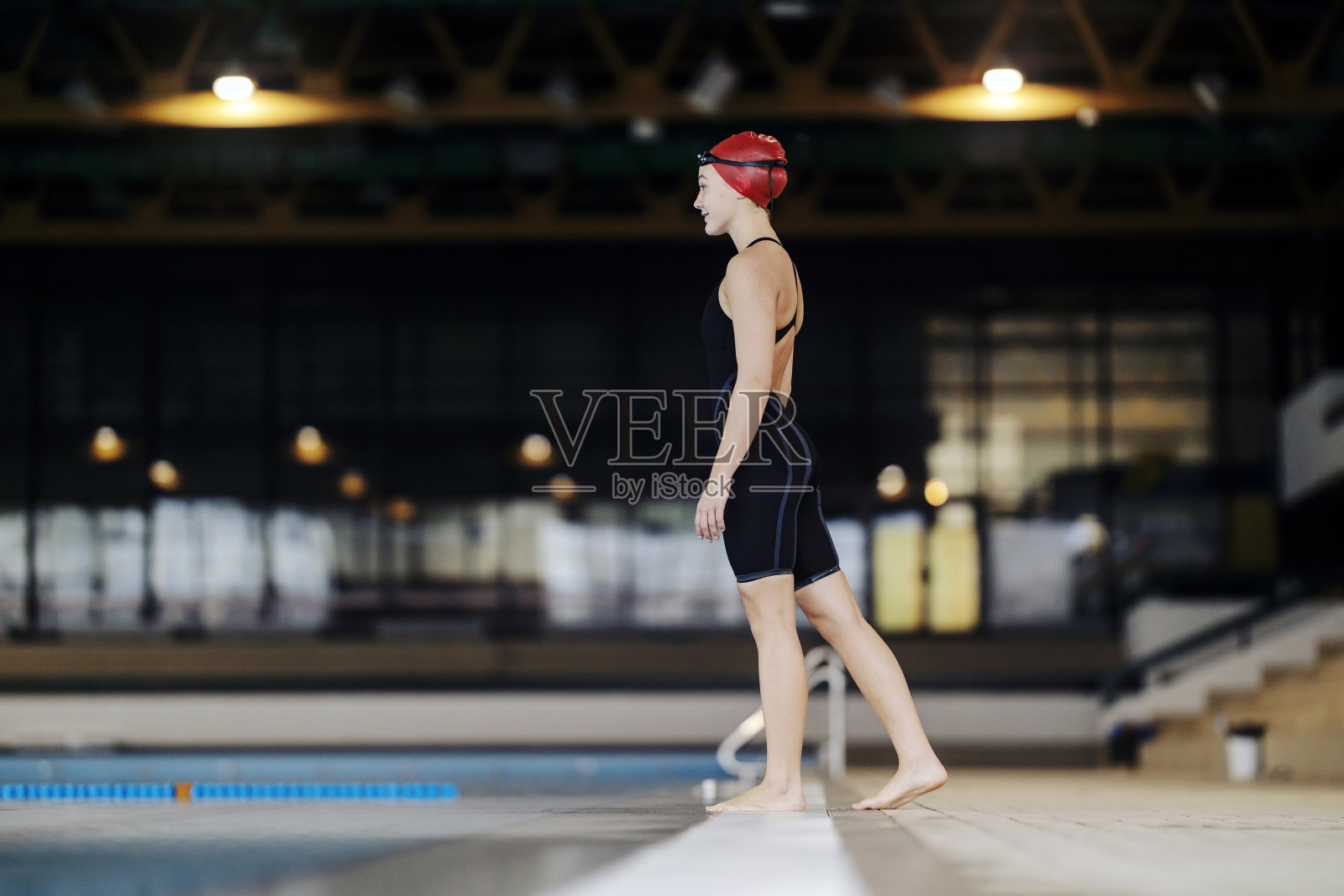 站在游泳池附近的专业游泳运动员的侧视图。照片摄影图片