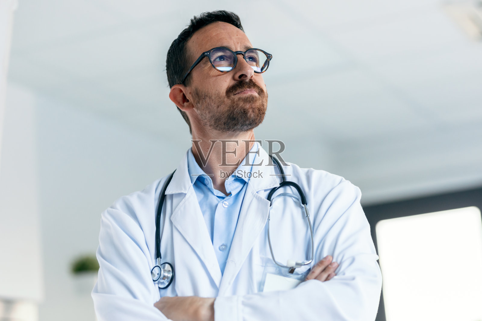 成熟的男医生脖子上戴着听诊器，在会诊时目光向前。照片摄影图片