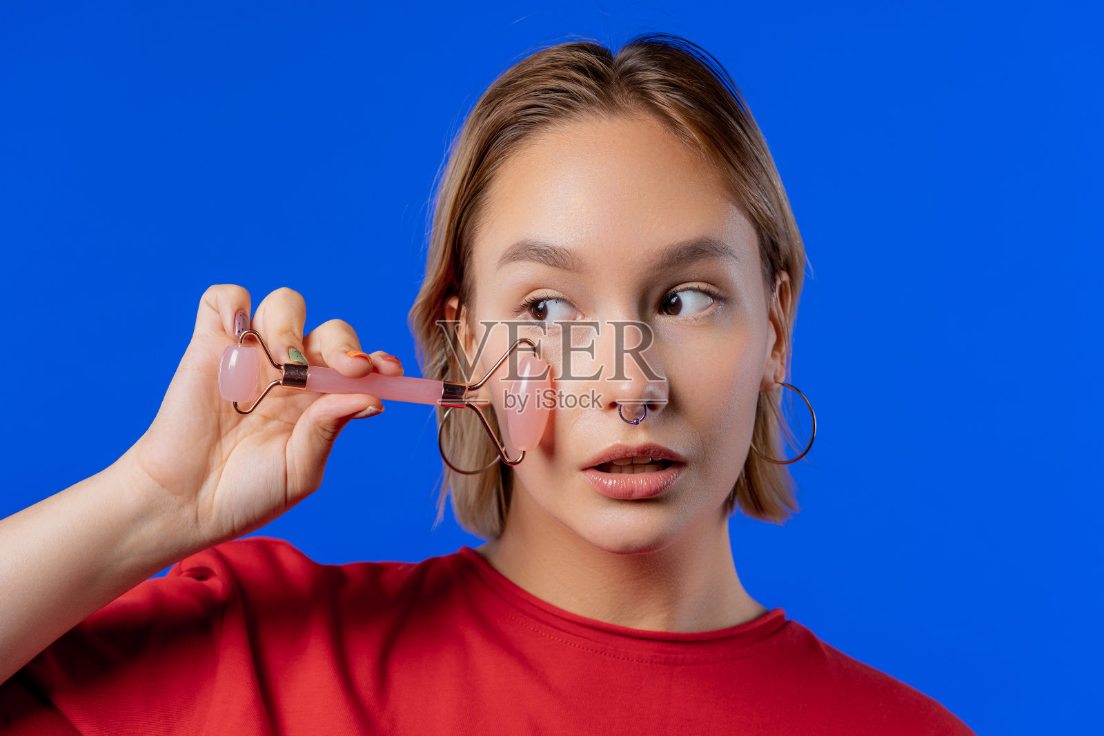 少女与玫瑰石英石辊在蓝色背景。面部自我护理照片摄影图片