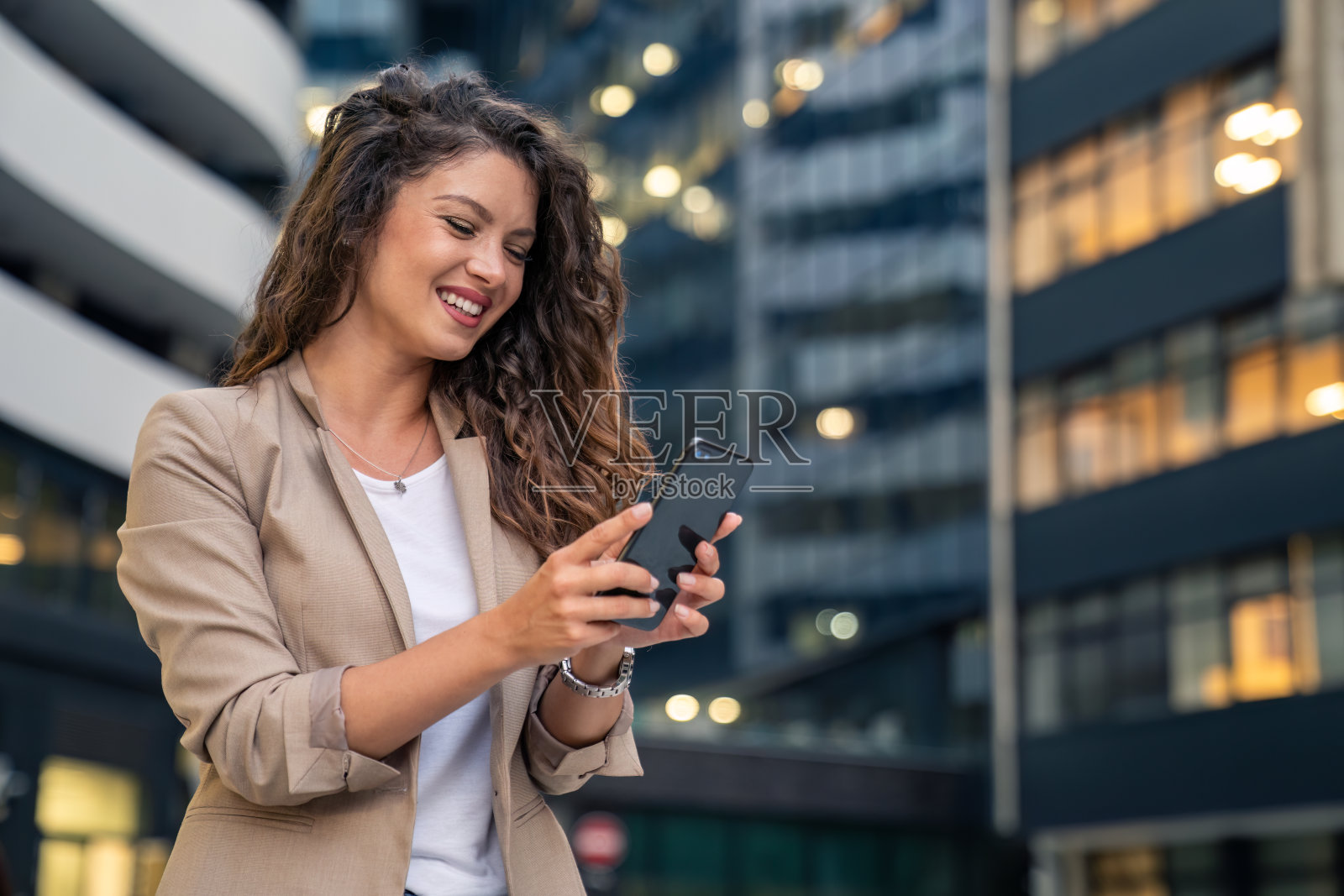 快乐微笑自信的女商人站在那里用智能手机发短信，用手机应用程序在外面工作照片摄影图片
