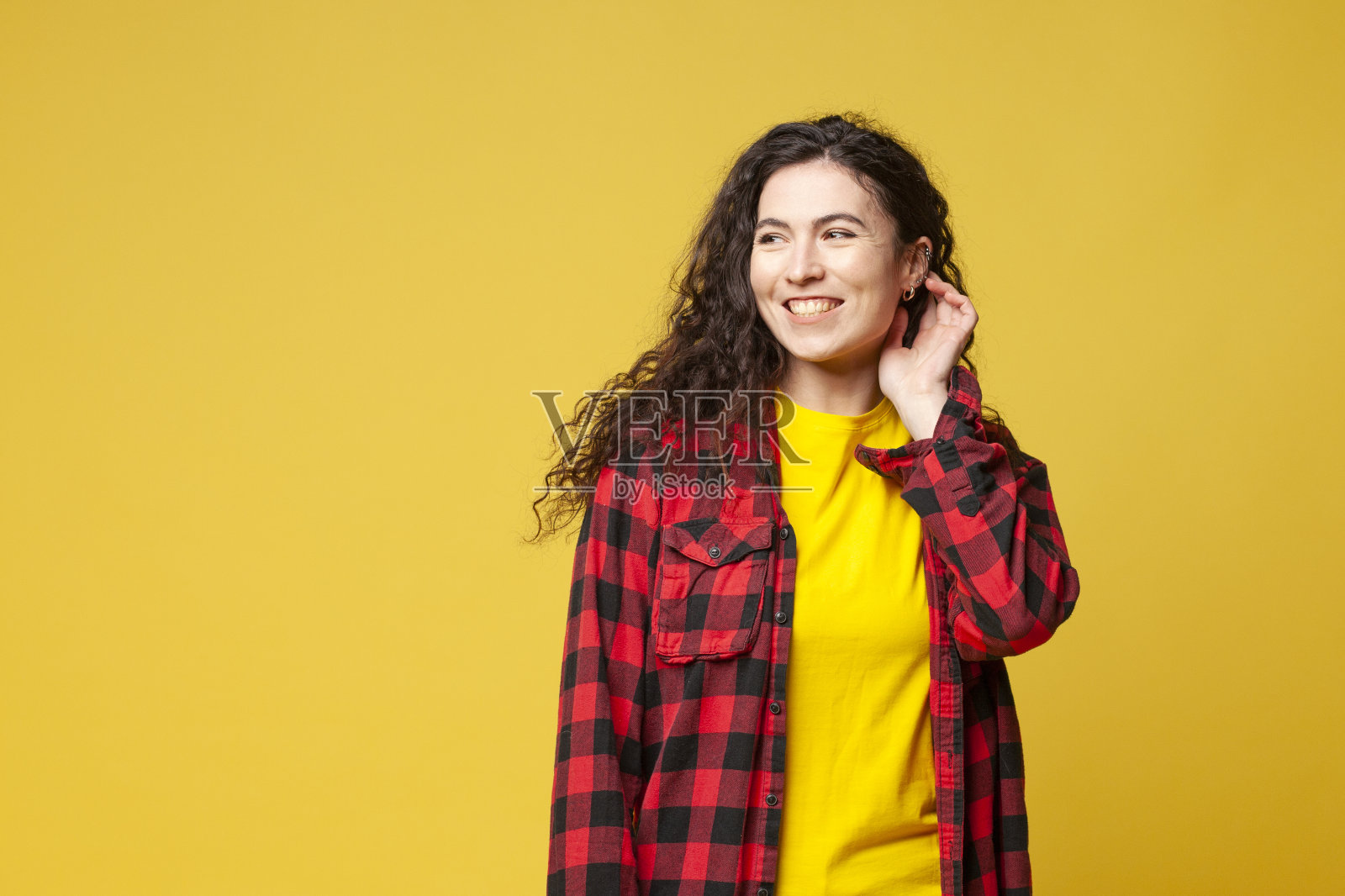 穿着格子衬衫的黑发卷发的年轻女孩站在黄色背景上微笑着，这是一幅年轻女学生的肖像照片摄影图片