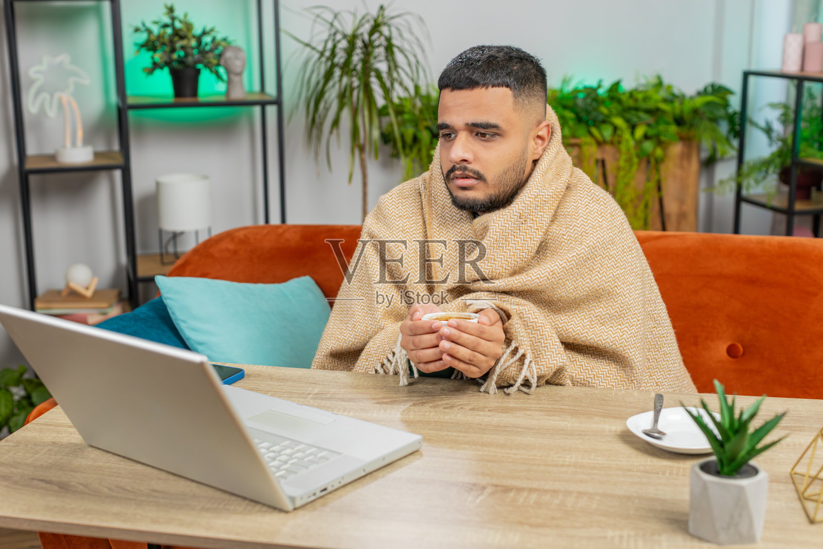 生病的印度自由职业者在用格子布包裹的笔记本电脑工作，坐在家里冻得瑟瑟发抖照片摄影图片