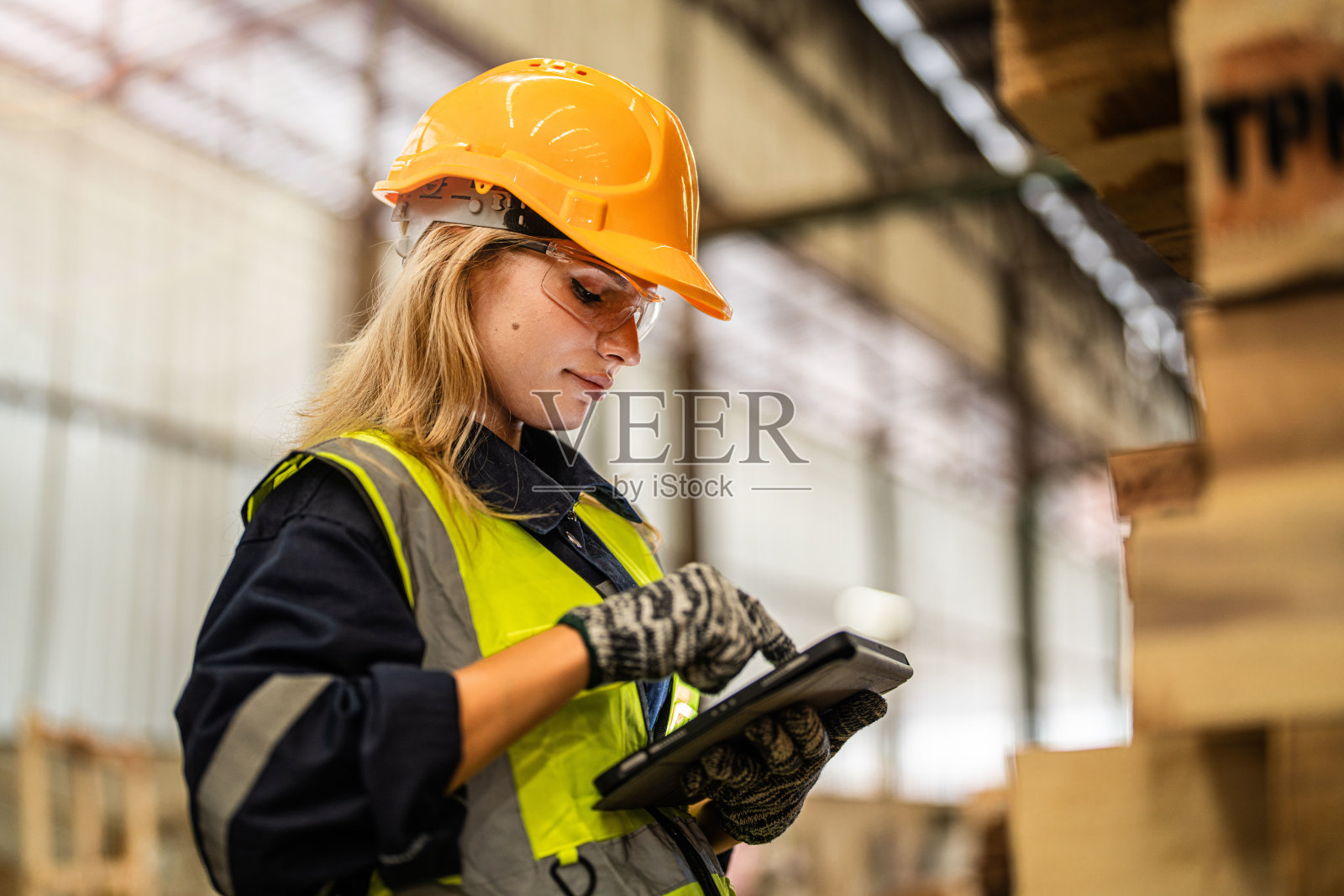 穿着安全制服，头戴安全帽的女工木匠，在车间生产中检查木制品的质量。男女工人在黑暗的仓库工业木材。照片摄影图片
