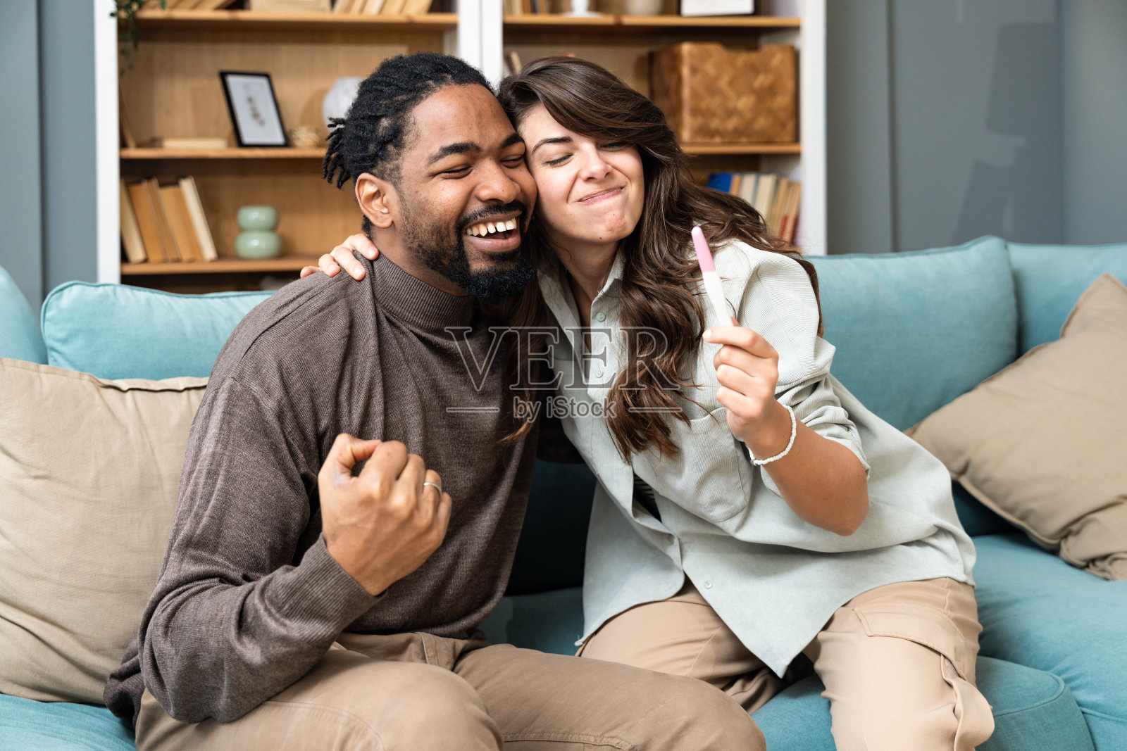 年轻夫妇期待怀孕测试结果呈阳性，计划成为父母并组建家庭。幸福的男人和怀孕的女人在沙发上拥抱照片摄影图片