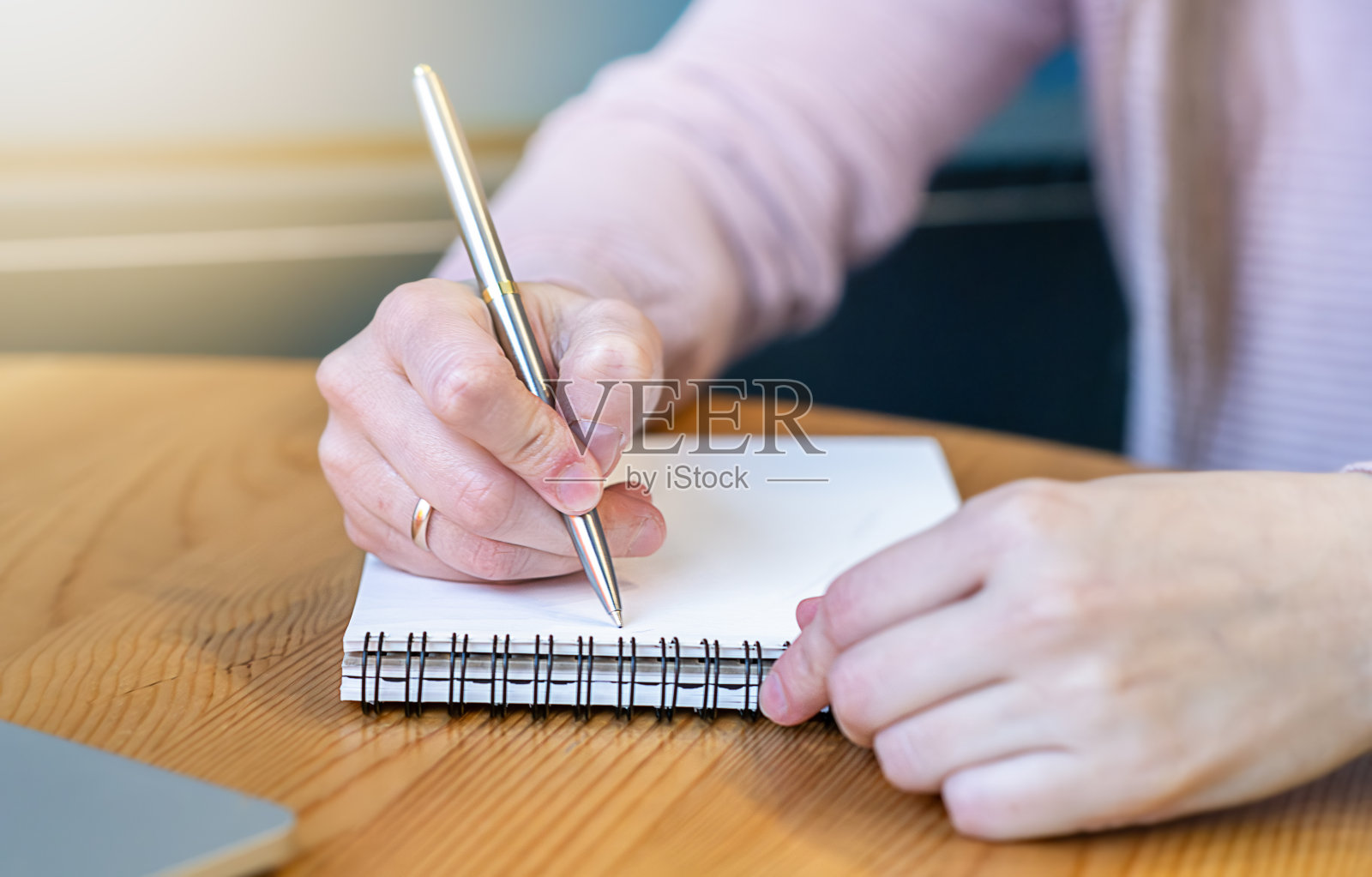 在笔记本上写下新年的目标、计划和愿望清单。寒假圣诞节，女人在家里拿着笔在笔记本上写字。照片摄影图片