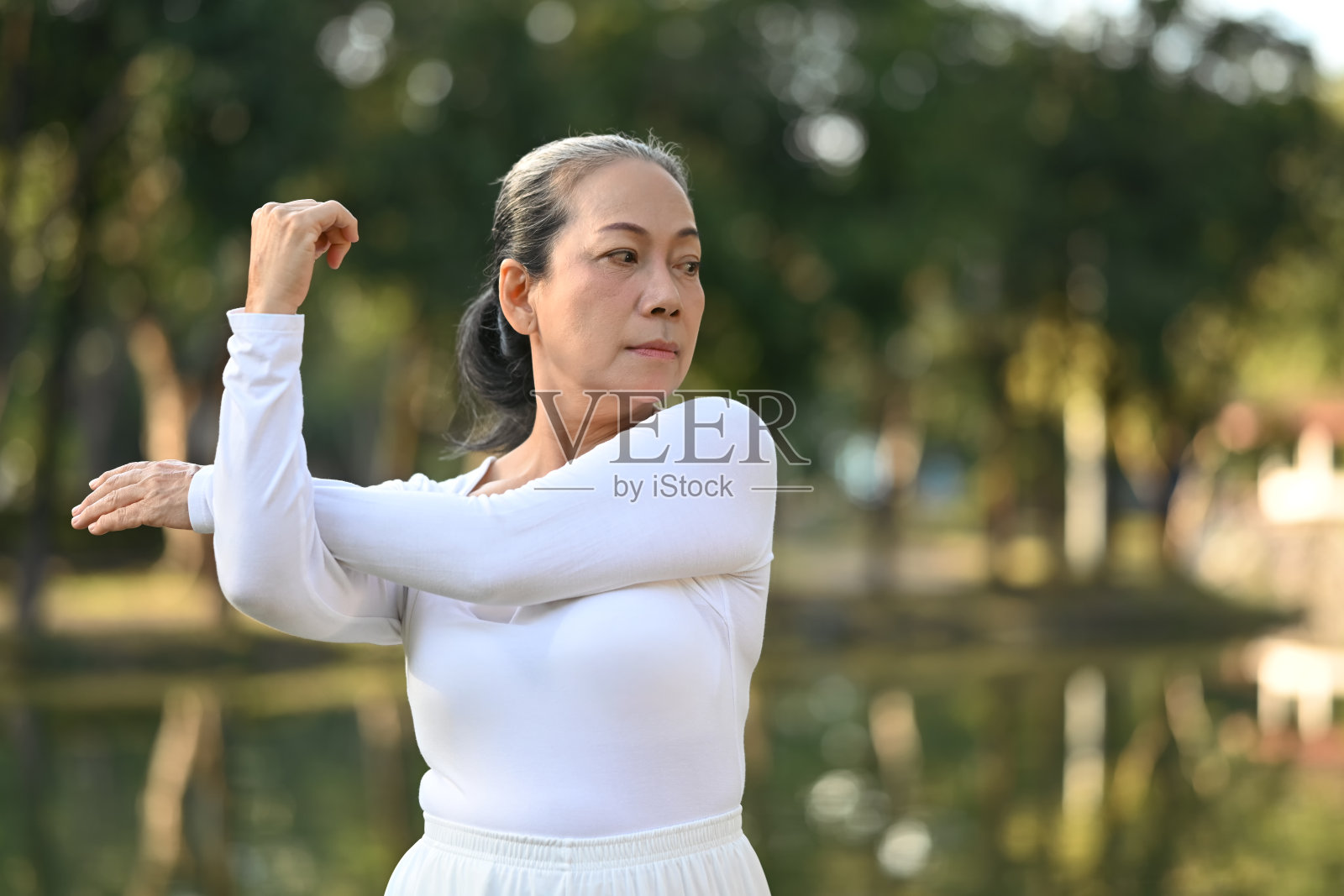 美丽的老年妇女在公园的裂缝附近伸展双臂，在退休期间保持健康。照片摄影图片