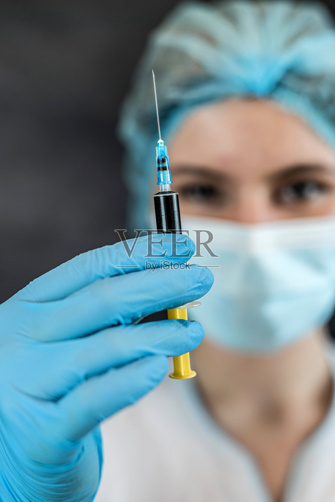 女护士或实习生穿着制服，戴着手套、口罩和帽子，手里拿着装有疫苗的注射器照片摄影图片