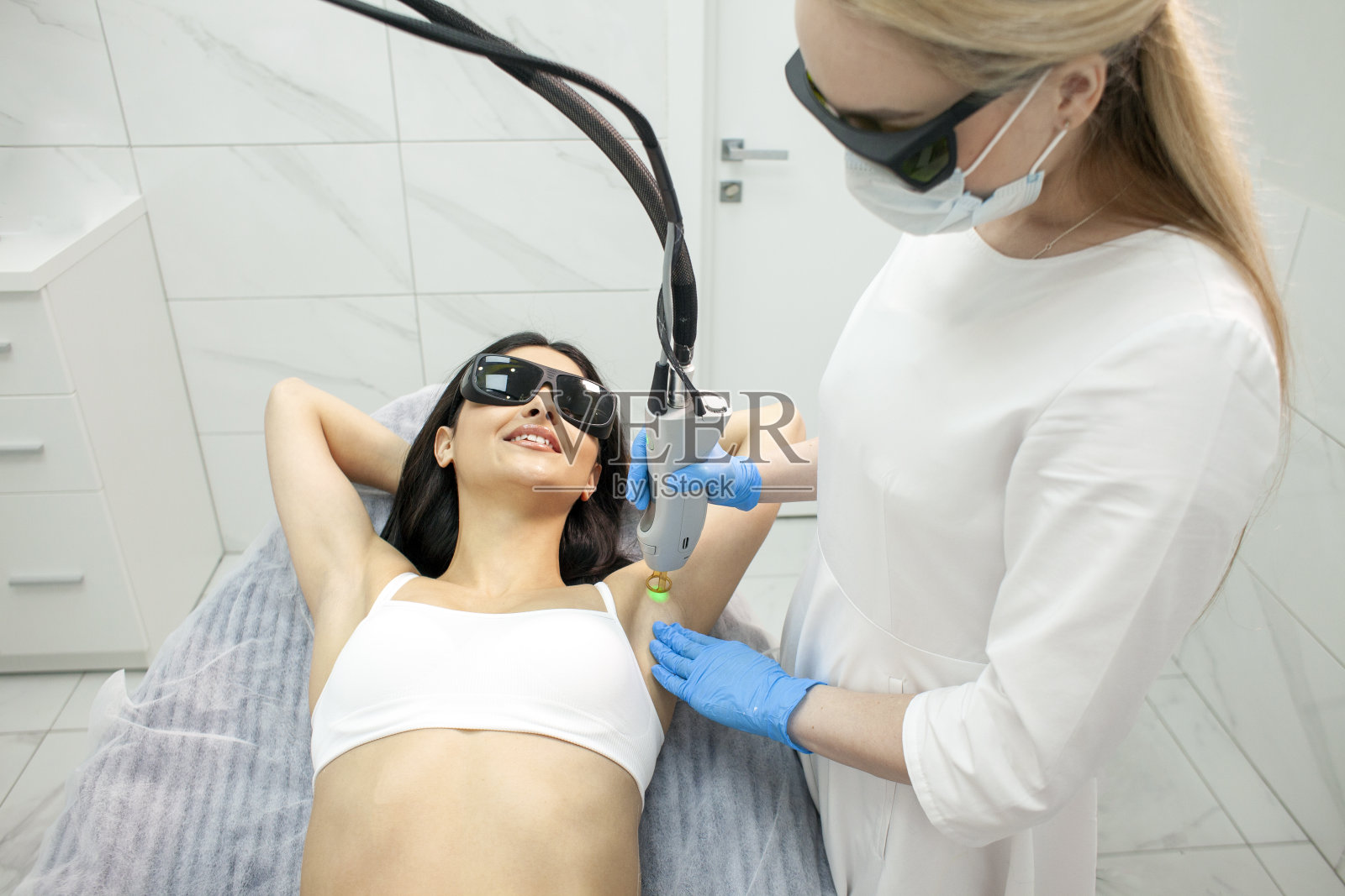 美容诊所腋窝脱毛。女病人用翠绿宝石激光做腋毛脱毛手术照片摄影图片