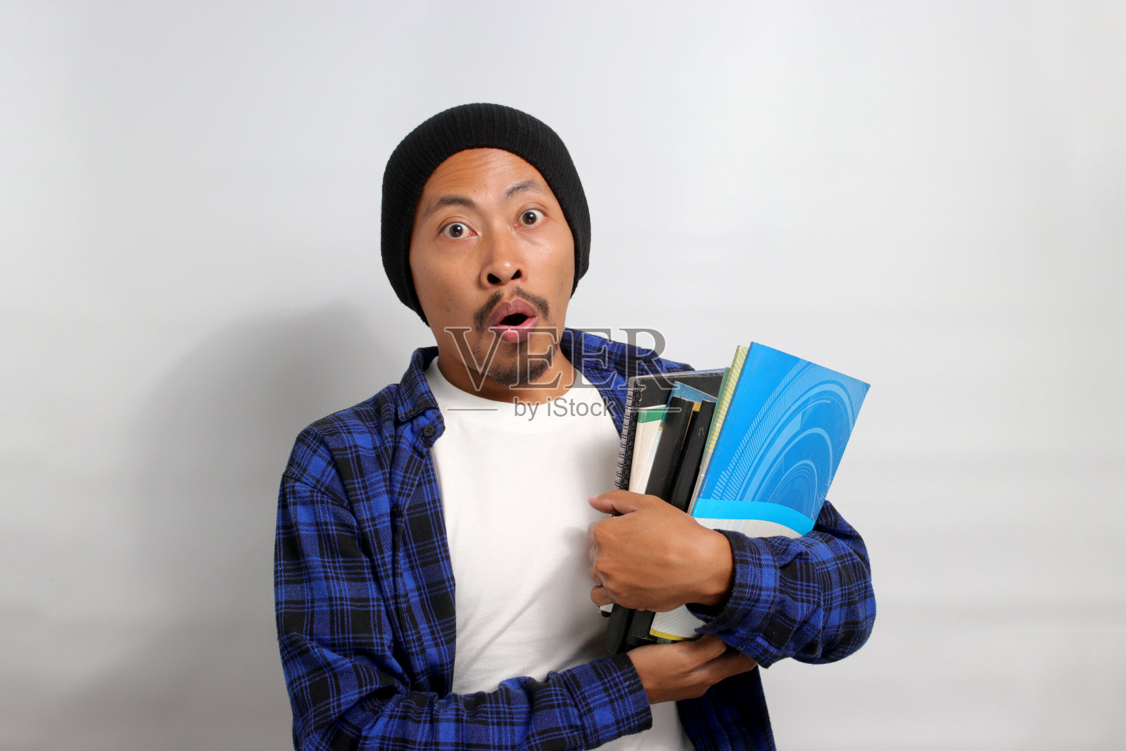 一位印象深刻的年轻亚洲男子拿着书，惊讶地张大嘴巴盯着镜头照片摄影图片