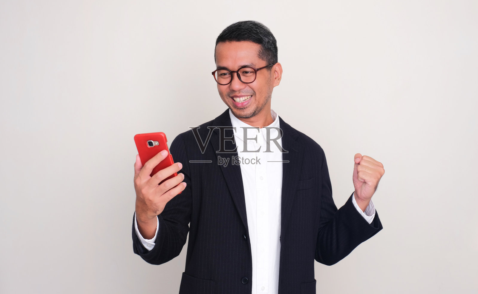 一个亚洲商人看着他的手机，微笑着握紧拳头照片摄影图片