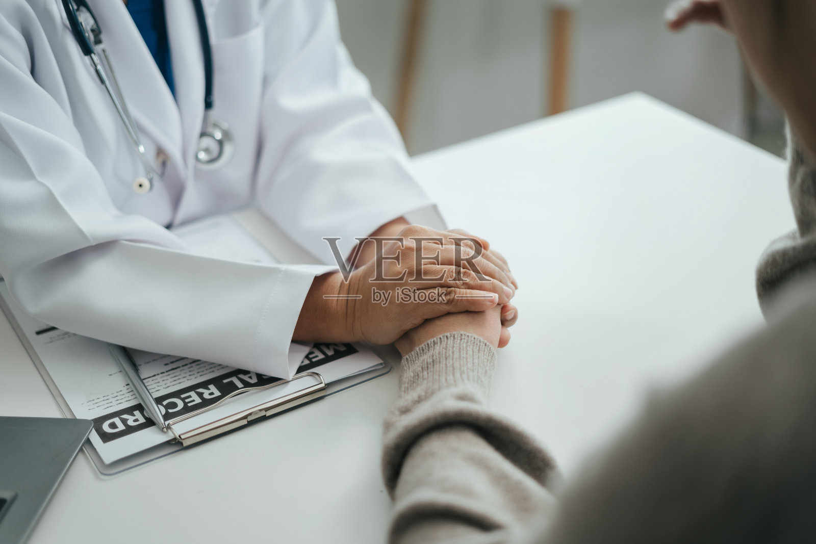 友好的女医生手握着病人的手，坐在办公桌前鼓励，同情，欢呼和支持，而医疗检查。照片摄影图片