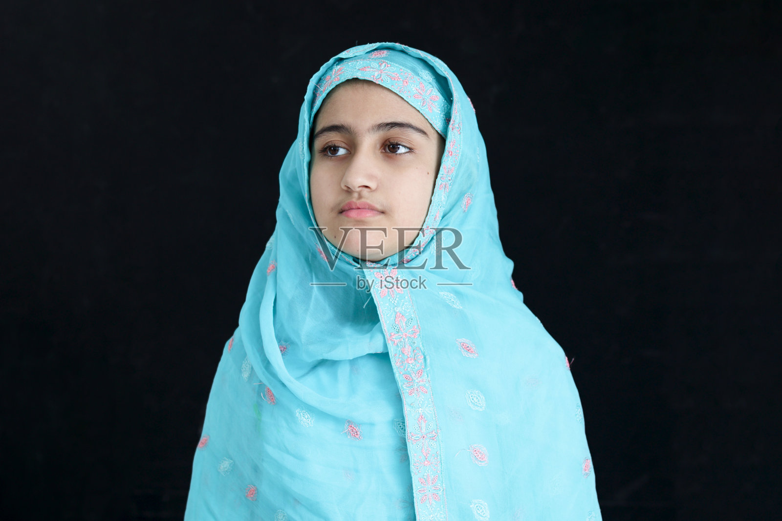 幸福微笑的印度穆斯林女孩肖像，穿着印度传统服装，戴着头巾，站在黑色背景上。女儿，小女孩，穿着蓝色的服装，有着美丽的眼睛。照片摄影图片