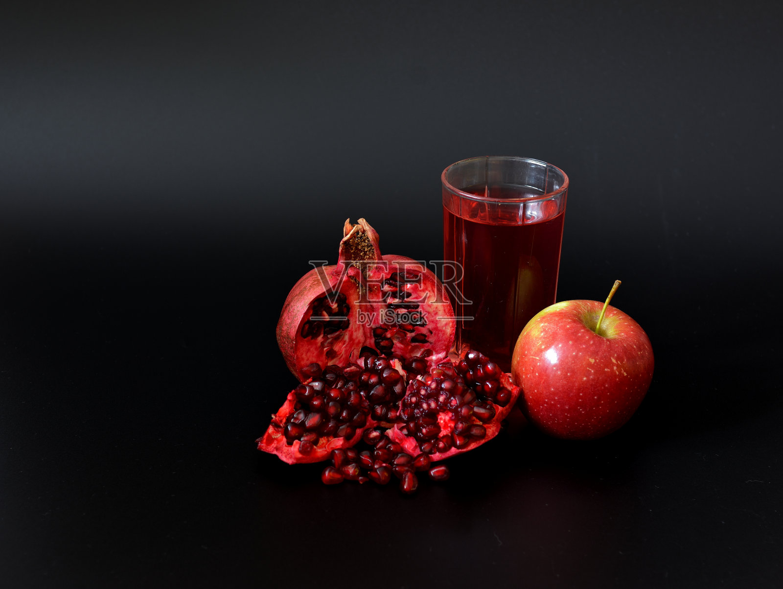 成熟的红苹果，碎石榴和一杯黑色背景的果汁。照片摄影图片