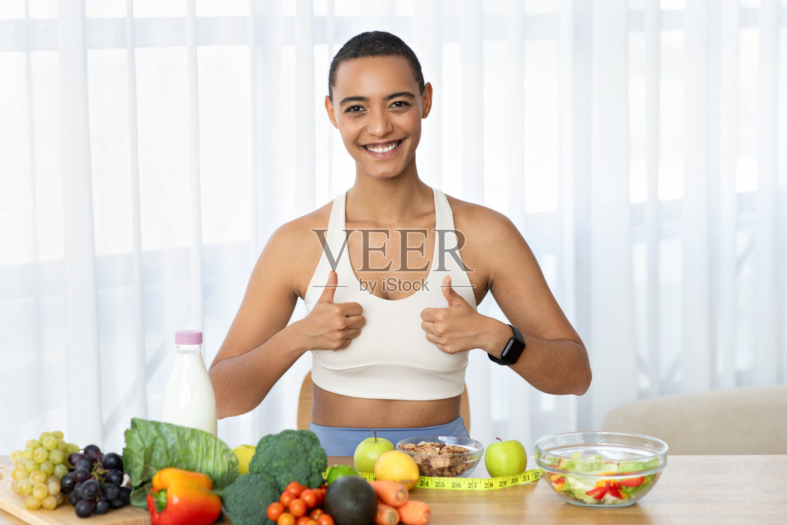 穿着运动服的快乐拉丁年轻女子在厨房灯光室内竖起大拇指照片摄影图片