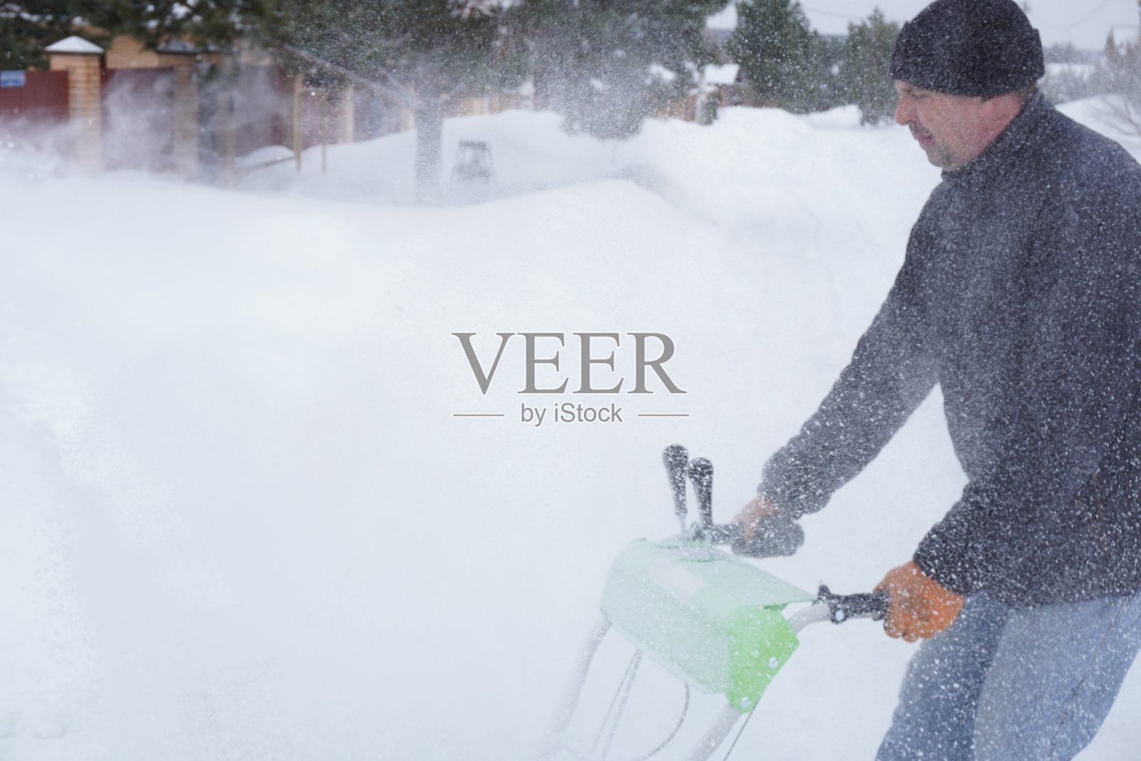 冬天，一个人在房子的院子里打扫雪，一个人用吹雪机打扫雪照片摄影图片