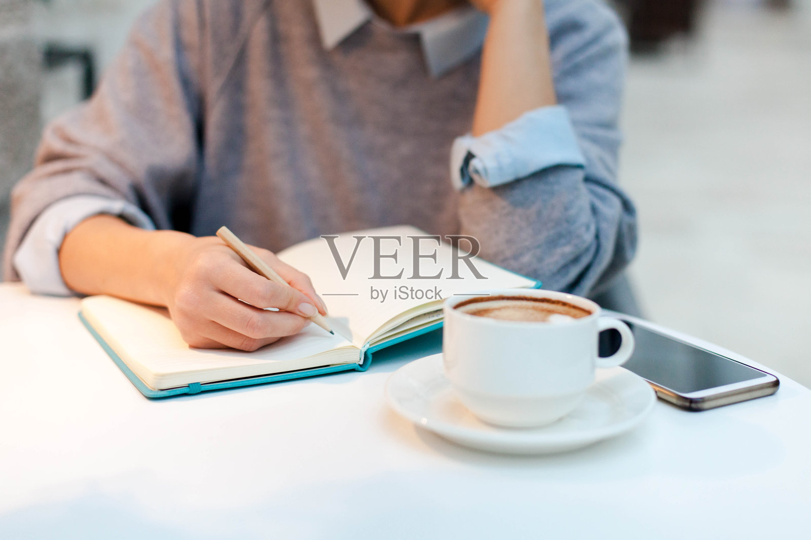 年轻女子在纸质笔记本上写着早晨的内容。女孩端着一杯咖啡坐在桌边照片摄影图片