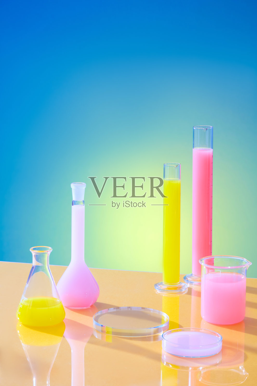 黄色和粉红色的液体在试管，培养皿和实验室烧瓶在蓝色梯度背景。产品展示空间。广告的复制空间。照片摄影图片