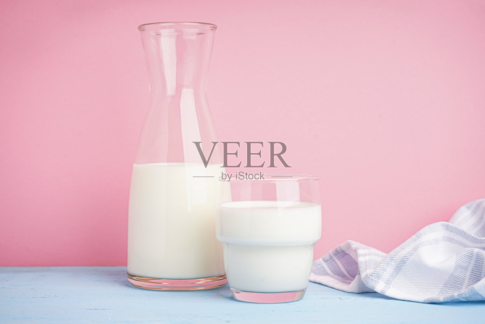 浅粉色背景的玻璃瓶和一杯鲜牛奶。照片摄影图片