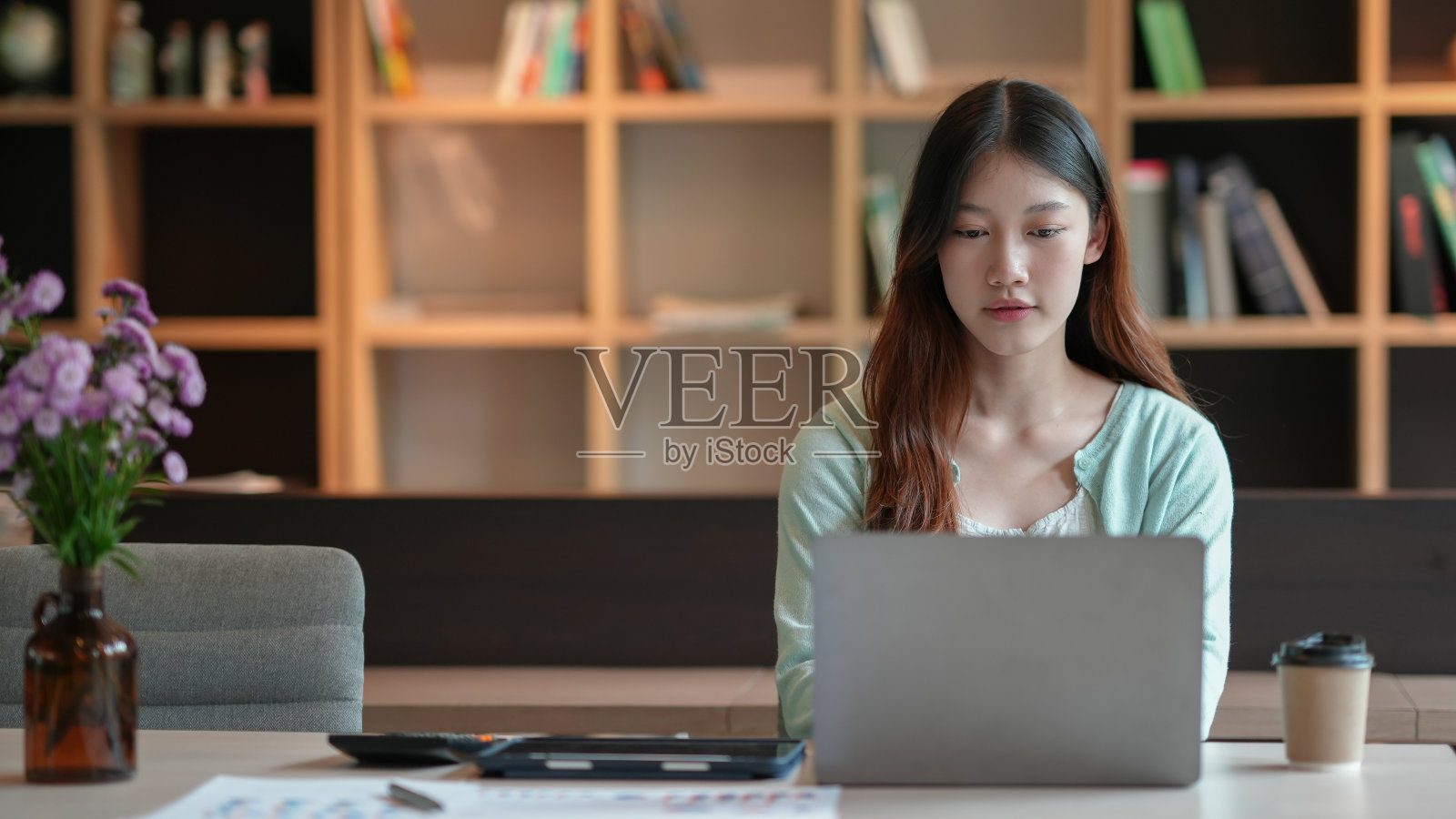 漂亮的年轻亚洲女学生在大学图书馆的桌子上愉快地用笔记本电脑工作。照片摄影图片
