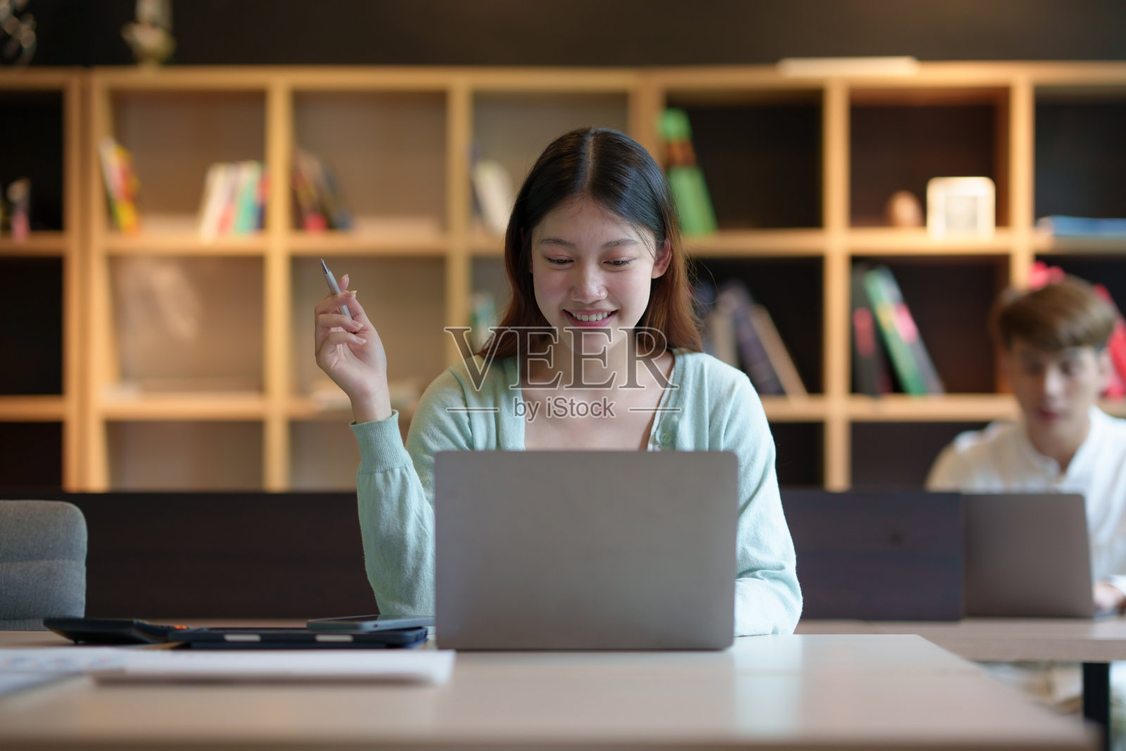 漂亮的年轻亚洲女学生在大学图书馆的桌子上愉快地用笔记本电脑工作。照片摄影图片
