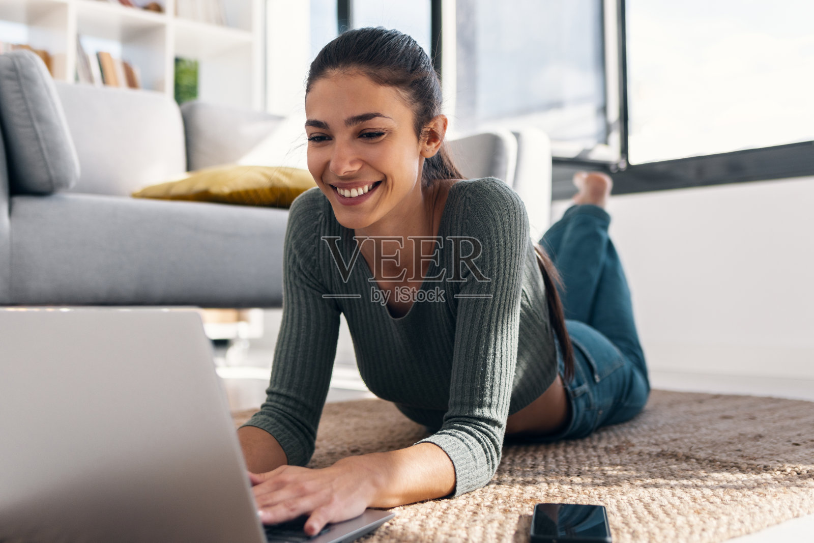 快乐的年轻女子躺在家里的地板上玩着她的笔记本电脑照片摄影图片